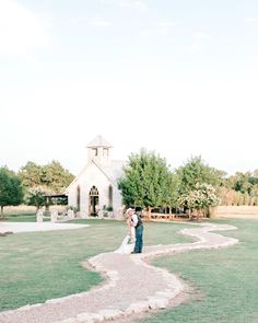 a bride and groom are standing in front of a white church on a grassy field