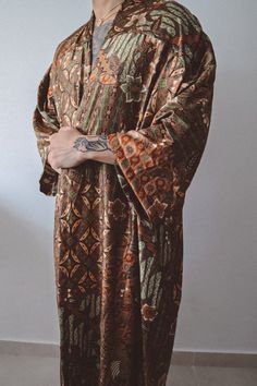 Mens Brown Gold Green Floral Kimono Robe: Sophisticated Design: Handcrafted long floor length kimono adorned with an elegant brown floral pattern complemented by refined gold and green accents for a luxurious touch. Size: Model normally wears size S.  Kimono can fit XS/S/M/L Silk Elegance: Crafted with exquisite silk blend fabric in a sleek brown hue, intricately woven with a stunning floral design for a chic and opulent appearance. Open-Front Style: Provides a relaxed, graceful fit, blending tr Brown Long Kimono For Festival, Long Brown Kimono For Festival, Traditional Brown Kimono For Festival, Traditional Long Sleeve Kurta For Loungewear, Long Sleeve Dabka Kimono For Eid, Traditional Long Brown Kurta, Bohemian Long Sleeve Kimono For Eid, Traditional Kimono Sleeve Festival Robe, Traditional Long Brown Kimono