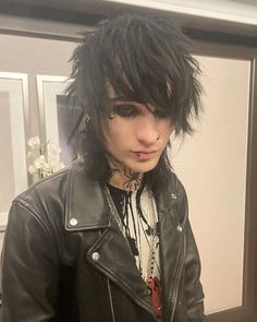 a man with black hair and piercings wearing a leather jacket in front of a mirror