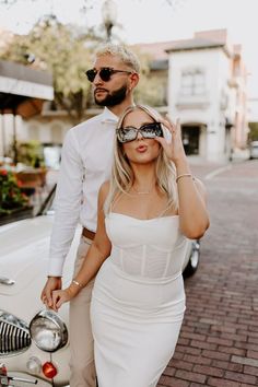 a man and woman standing next to each other in front of a white vintage car