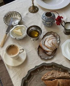 an assortment of breads, tea and butter on a white tablecloth with silver dishes