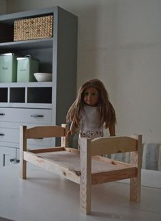 a doll sitting on a wooden bed frame in a room with white cabinets and drawers