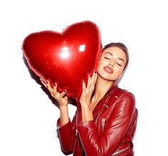 a woman holding a red heart shaped balloon in her right hand and covering her face with both hands