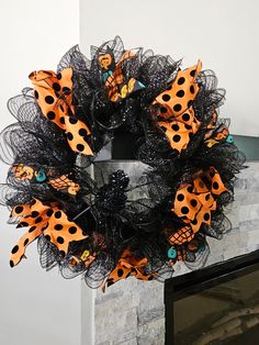 a black wreath with orange and black polka dots on it sitting in front of a fireplace