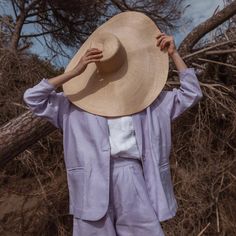 a woman with a hat on her head is standing in front of some dry grass