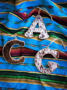 two wooden letters sitting on top of a colorful cloth covered table with string attached to them