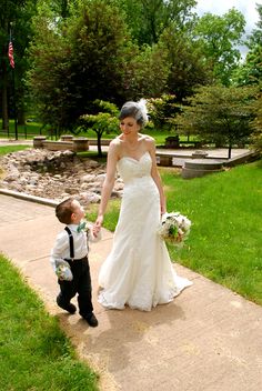 a woman in a wedding dress holding the hand of a young boy