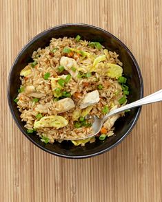 a black bowl filled with rice and vegetables on top of a wooden table next to a spoon