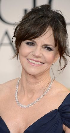 an older woman in a blue dress smiles at the camera while wearing a diamond necklace