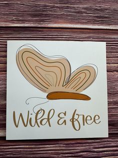 a greeting card with the words wild and free written on it in brown ink, sitting on a wooden surface