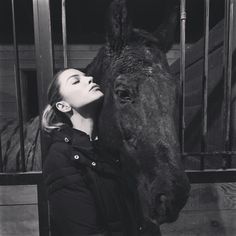 a woman standing next to a horse in a stable with it's head on the fence