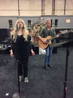 two people standing in front of microphones with guitars on the floor and one person holding a guitar