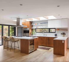 an open kitchen with wooden floors and white counter tops, along with two bar stools