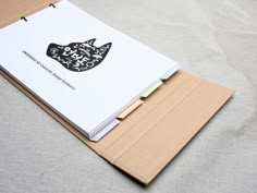 an open notebook with a cat design on the front and back cover sitting on top of a sheet of paper