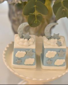 two small blue and white boxes with stars and clouds on them sitting on a plate next to a potted plant