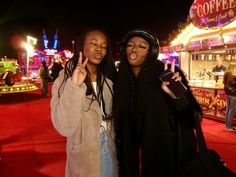 two women standing next to each other in front of a carnival ride at night time