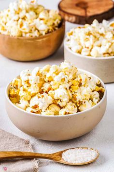 three bowls filled with popcorn sitting on top of a table next to wooden spoons