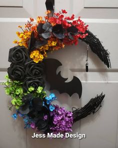 a halloween wreath with flowers and bats hanging on the front door, decorated with fake flowers