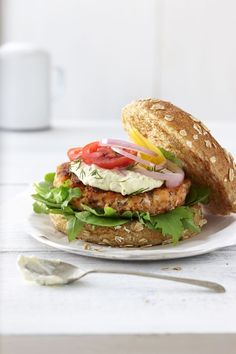 a chicken burger with lettuce, tomato and mayonnaise on a white plate