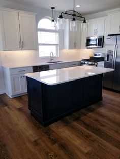 a large kitchen with an island in the middle and white cabinets on both sides, along with stainless steel appliances