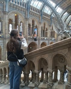 a woman taking a photo of the skeleton of a dinosaur in a museum with her cell phone