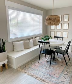 a dining room table with four chairs next to a white bench and potted plants