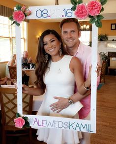 a man and woman pose for a photo in front of a floral frame