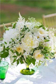 white flowers in green vases sitting on a table with an empty glass next to it