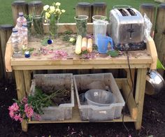 a wooden table topped with pots and pans filled with flowers next to a metal toaster