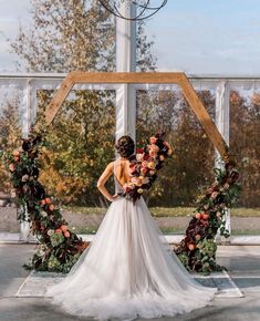 a woman wearing a wedding dress standing in front of an arch with flowers on it