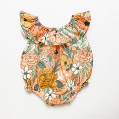 an orange floral romper with ruffles on the front and bottom, sitting on a white surface