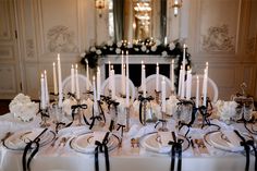 the table is set with white flowers and black ribboned napkins, candles, and plates