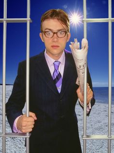 a man in a suit and tie behind bars holding up a piece of paper that looks like a newspaper