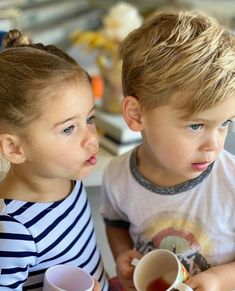 two young children sitting next to each other holding cups