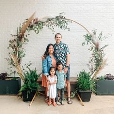 a family posing for a photo in front of an arch with greenery and potted plants