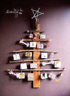 a christmas tree made out of wooden sticks with pictures pinned to it's sides