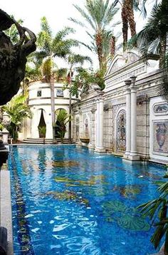 an outdoor swimming pool surrounded by palm trees and other greenery in front of a white building