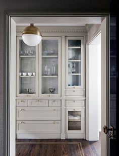 a white china cabinet with glass doors in a room that has hardwood floors and walls