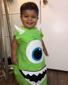 a little boy dressed up in a green monster costume with big blue eyes and horns