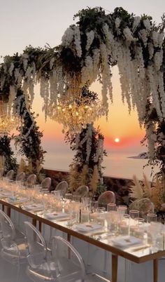 an outdoor dining area with white flowers and greenery on the table, overlooking the ocean