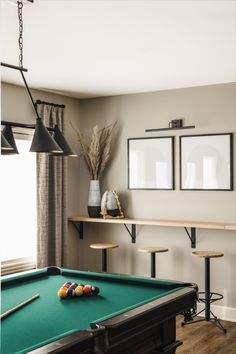 a pool table in a room with two pictures on the wall and three stools