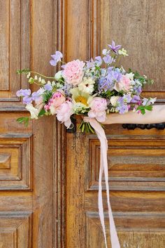 a bouquet of flowers on the arm of a woman in front of a wooden door