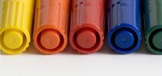 six different colors of crayons lined up in a row on a white surface