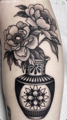 a black and white tattoo with flowers in a vase on the thigh, done by person