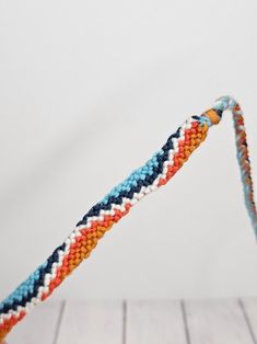 an orange, blue and white crocheted object on a wooden table with a string attached to it