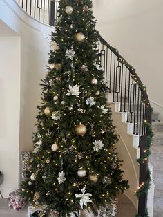 a decorated christmas tree in front of a spiral staircase