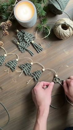 someone is making christmas decorations with twine on the table next to yarn, pine cones and candles