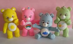 four different colored teddy bears sitting next to each other on a pink surface with one bear holding a rainbow ball