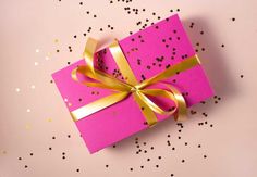 a pink gift box with gold ribbon and confetti sprinkles around it