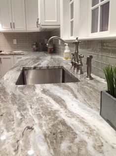 a granite counter top in a kitchen with white cabinets and stainless steel sink faucet